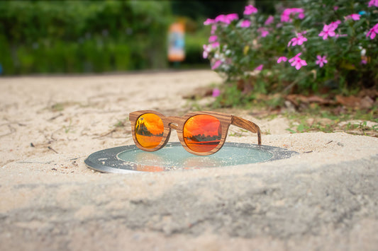 MoovWave BlooWave Ember wooden floatable polarized sunglasses with orange lenses resting on sandy ground outdoors