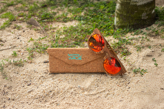 MoovWave BlooWave Ember wooden floatable polarized sunglasses with orange lenses on sandy beach beside a cork case
